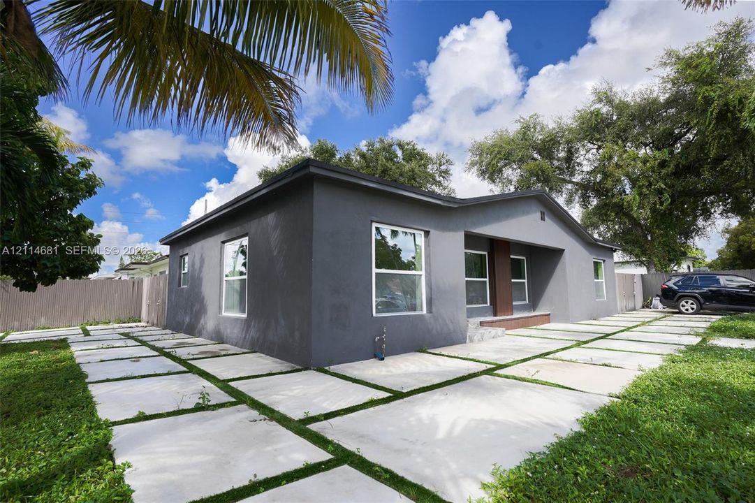Single-story exterior featuring a dark-toned stucco facade, grid-patterned concrete paver driveway, and a recessed entryway with a wooden accent pillar