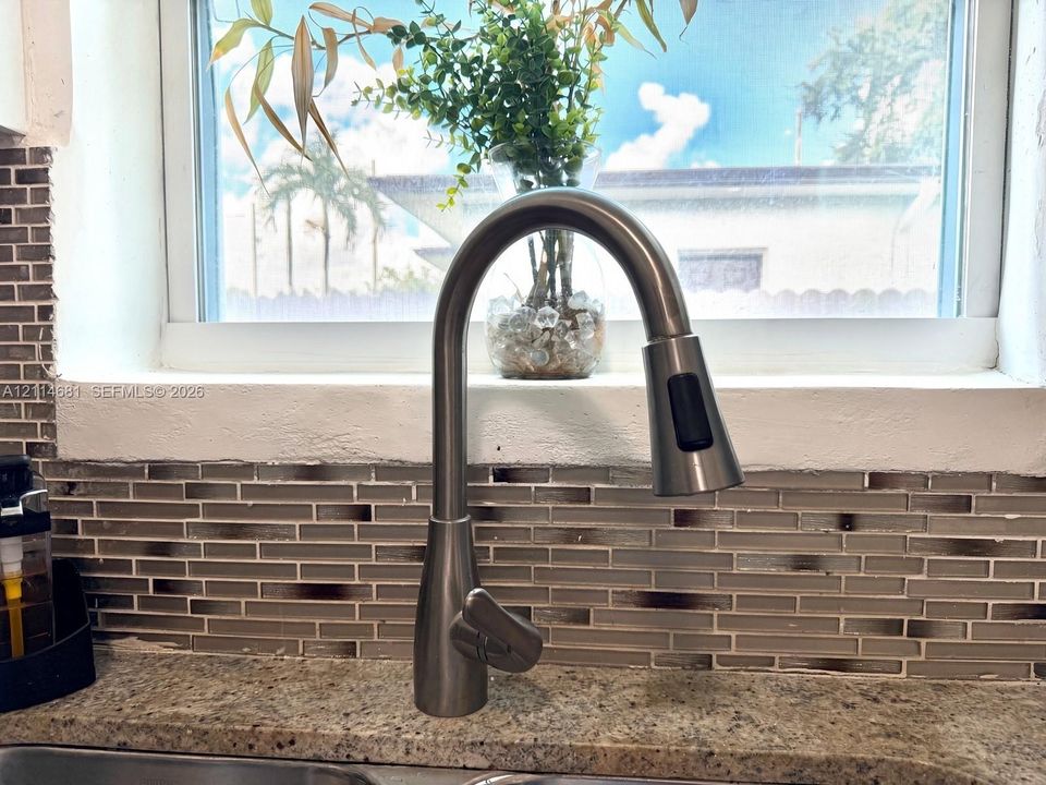 High-arc pull-down faucet with a brushed metallic finish, set against a multi-toned glass tile backsplash and stone countertop with an integrated basin