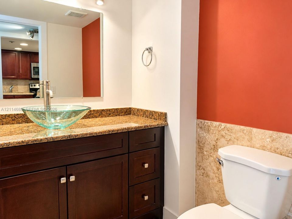 Bathroom featuring a dark wood vanity with stone countertop, glass vessel sink, chrome faucet, and tile wainscoting