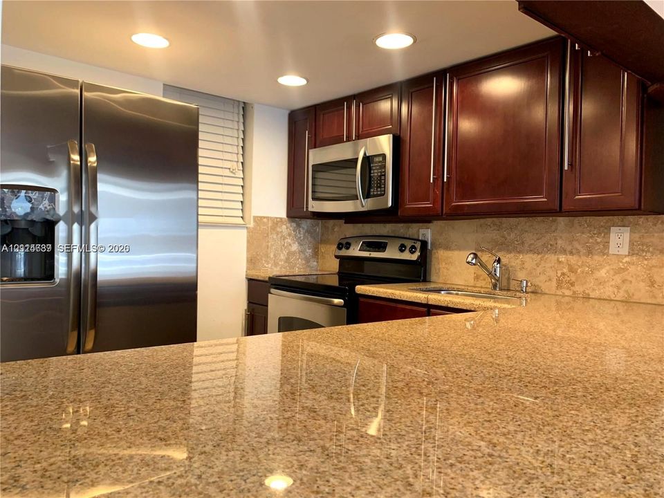 Kitchen featuring stone countertops, dark wood-finish cabinetry, stainless steel appliances, a stone tile backsplash, and recessed lighting