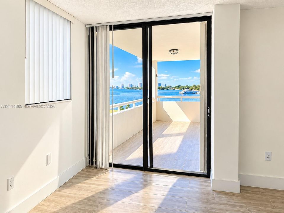 Sliding glass doors opening to a private balcony featuring ceramic tile flooring, a solid railing, and water frontage