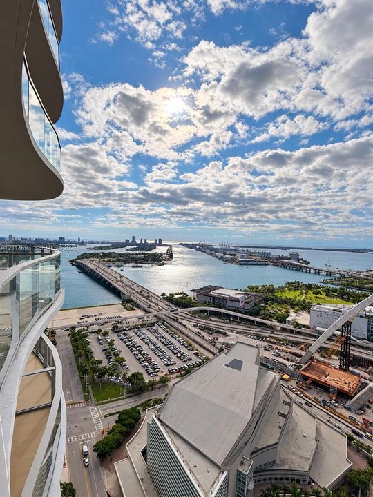 Curved balcony featuring tempered glass railings overlooking a coastal cityscape and harbor