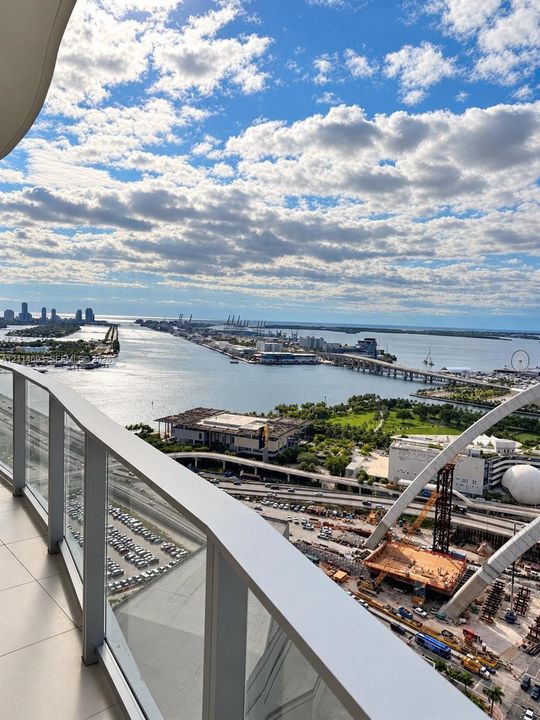 Private balcony featuring glass panel railing and tile flooring, offering a wide-angle perspective of the harbor, bridges, and surrounding cityscape