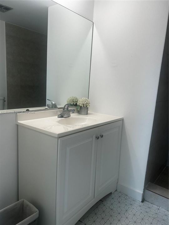 Bathroom vanity featuring white shaker-style cabinetry, an integrated basin, a polished chrome faucet, and a large wall-mounted mirror over geometric-patterned tile flooring