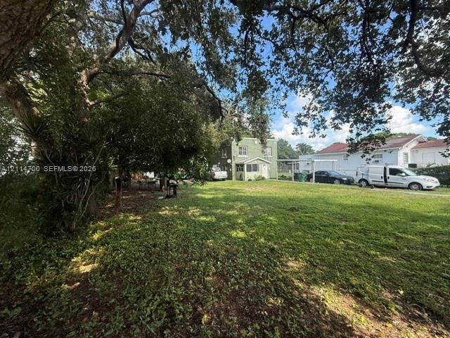 Expansive lawn area featuring mature canopy trees and a structural carport