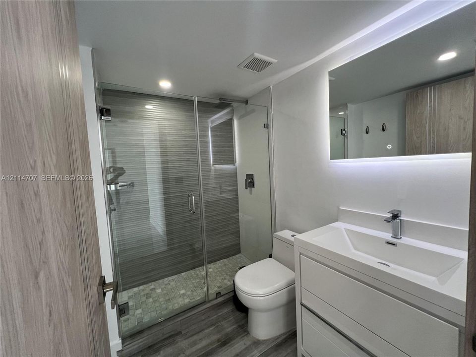Modern bathroom featuring a glass-enclosed walk-in shower with horizontal tile surround, a built-in vanity with a rectangular sink, wood-finish cabinetry, and an integrated LED-lit mirror