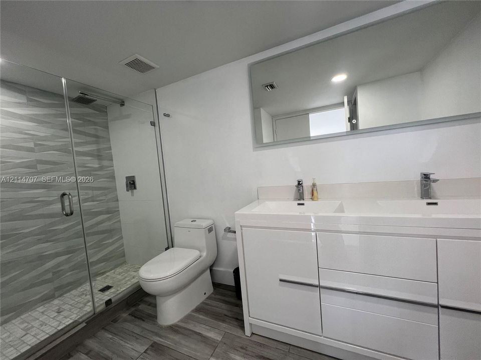 Double vanity with integrated sinks, glass-enclosed shower featuring textured wall tile, mosaic tile shower floor, and wood-finish flooring