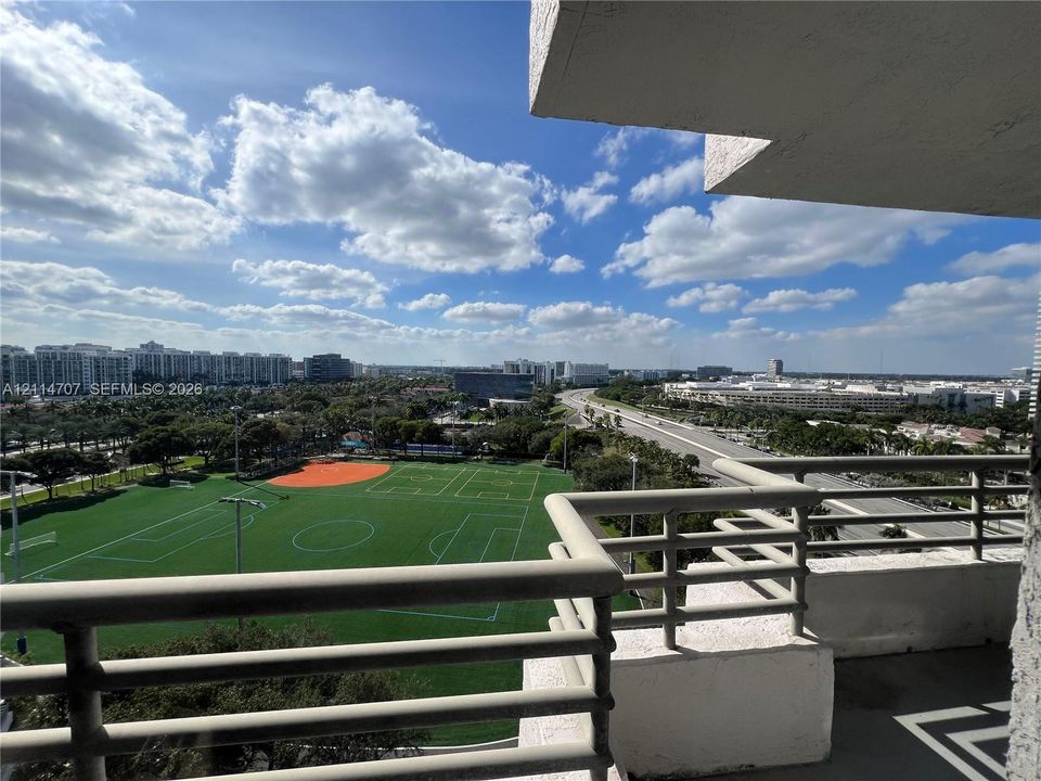 Private balcony with metal railings overlooking an athletic complex and municipal landscape
