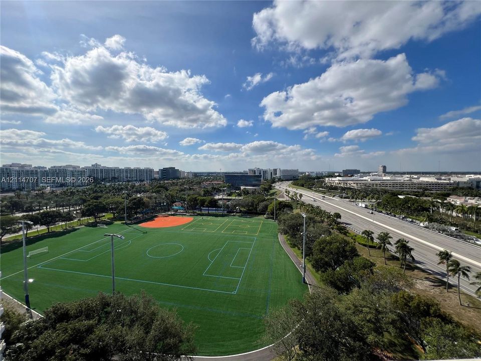 Elevated aerial perspective featuring a multi-sport turf field with integrated markings, perimeter lighting, and paved walking paths