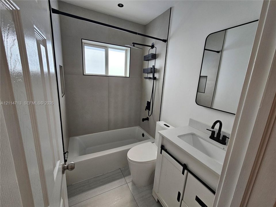 Bathroom featuring large-format gray tile surround, matte black plumbing fixtures, white vanity with integrated basin, and arched wall-mounted mirror