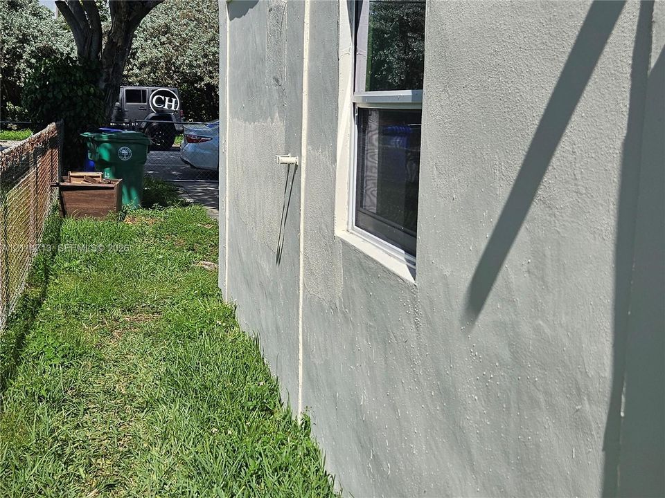 Stucco exterior wall featuring a single-pane aluminum-framed window and chain-link perimeter fencing