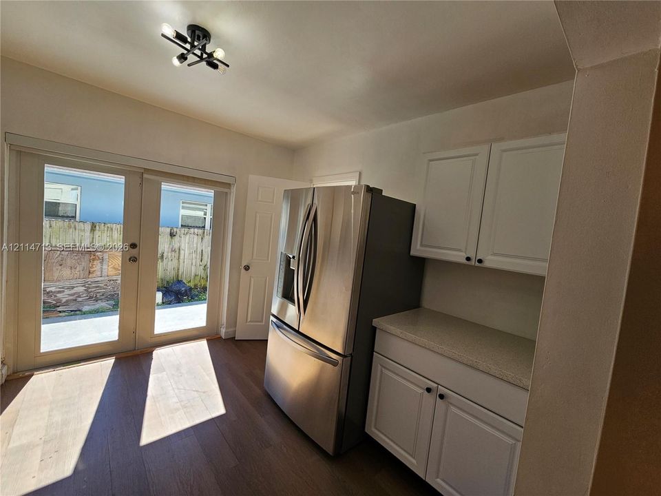 Kitchen featuring wood-finish flooring, white cabinetry, a solid-surface countertop, stainless steel refrigerator, and glass-paneled double doors