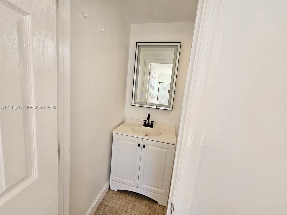 White vanity cabinet featuring an integrated sink, stone-finish countertop, matte black faucet, and a rectangular mirror