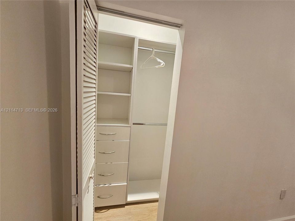 Closet featuring custom white built-in shelving, a series of four integrated drawers, a metal hanging rod, and a louvered door