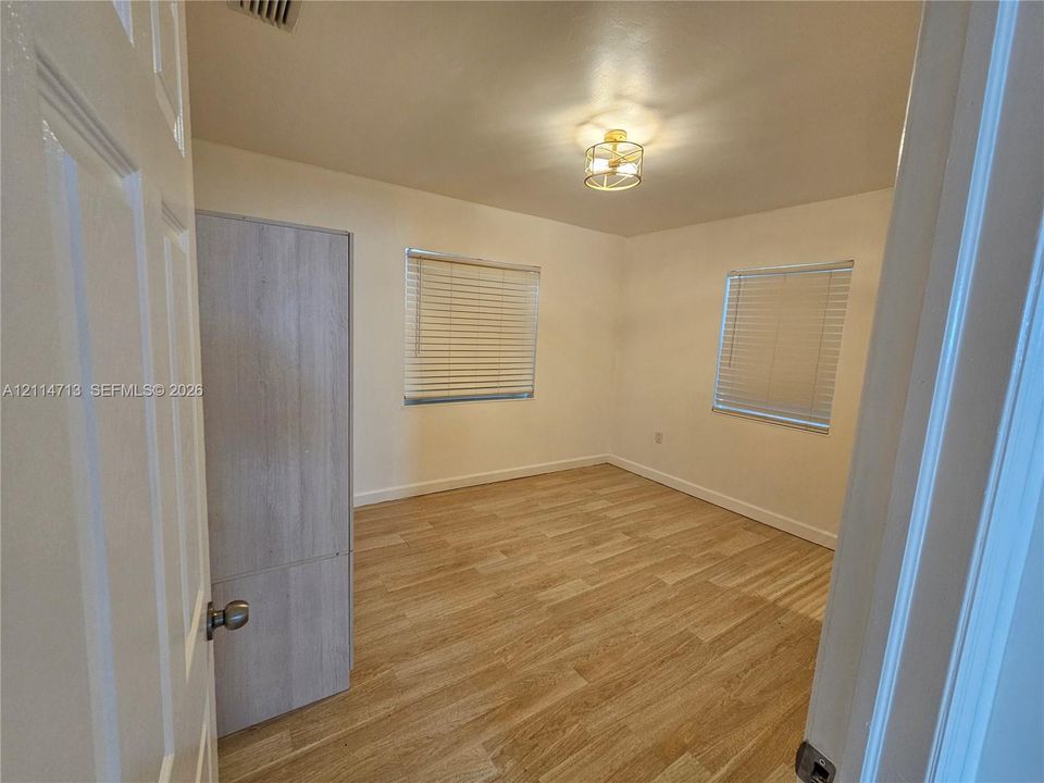 Room featuring wood-finish flooring, two windows with horizontal blinds, and a drum-style ceiling light fixture