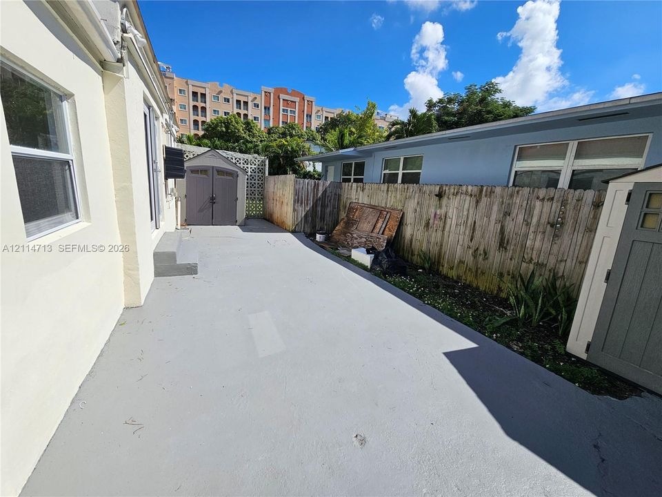 Exterior concrete patio featuring dual storage structures, perimeter wood fencing, and fixed exterior wall-mounted lighting