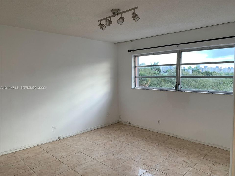 Room featuring tile flooring, adjustable multi-head track lighting, and a window with exterior urban scenery