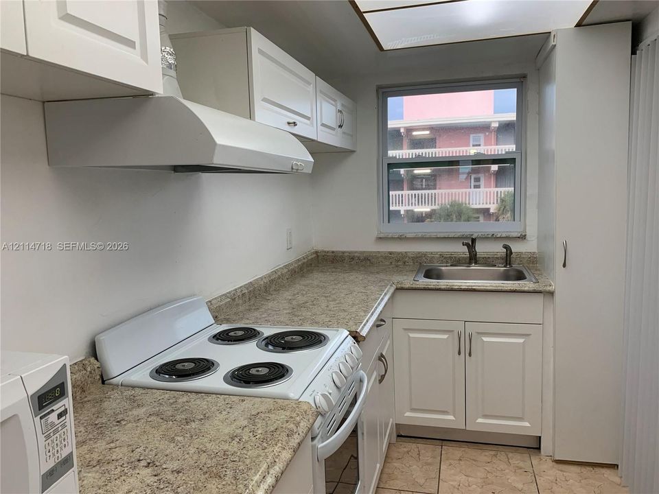 Kitchen featuring white cabinetry, stone-finish countertops, stainless steel sink with a high-arc faucet, white electric range, and tile flooring