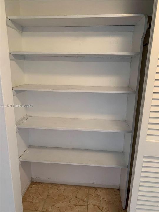 Built-in closet featuring four fixed white shelving tiers and louvered folding doors