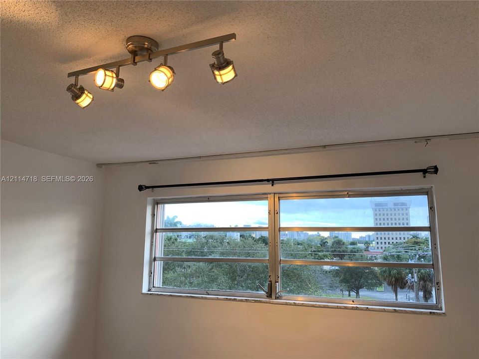 Multi-light ceiling-mounted track fixture with a metallic finish and horizontal louvered windows providing exterior city and landscape scenery