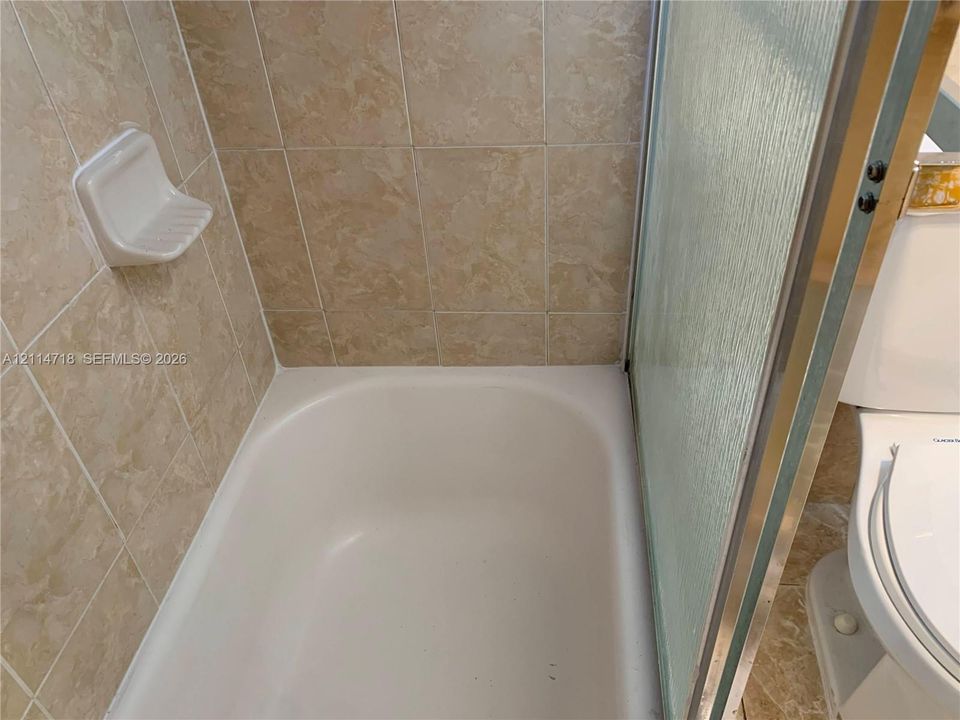 Bathtub with neutral-toned wall tiling, integrated soap dish, and glass sliding shower door