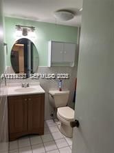 Bathroom featuring a wood-finish vanity with an integrated sink, oval wall-mounted mirror, white wall-mounted cabinet, and tile flooring