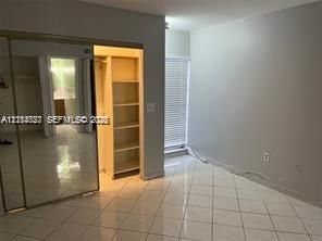 Ceramic tile flooring, built-in floor-to-ceiling shelving, mirrored sliding closet doors, and horizontal window blinds
