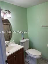 Bathroom featuring wood-finish vanity cabinetry, oval wall-mounted mirror, three-light polished chrome fixture, and white porcelain sink