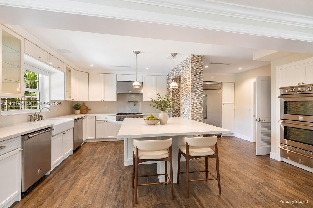 Kitchen featuring white cabinetry, an expansive central island with a solid surface countertop, wood-finish flooring, stainless steel built-in double ovens, and decorative tile accent wall