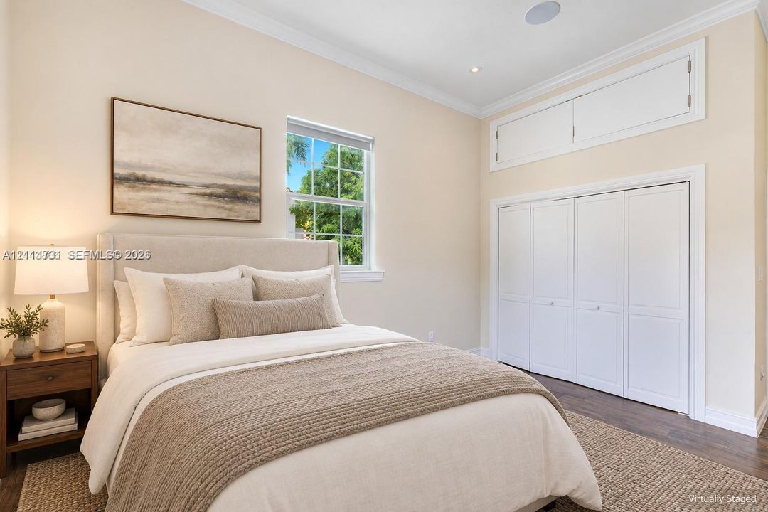 Neutral-toned room featuring dark wood-finish flooring, white bi-fold closet doors, additional overhead storage cabinetry, and a window with exterior greenery