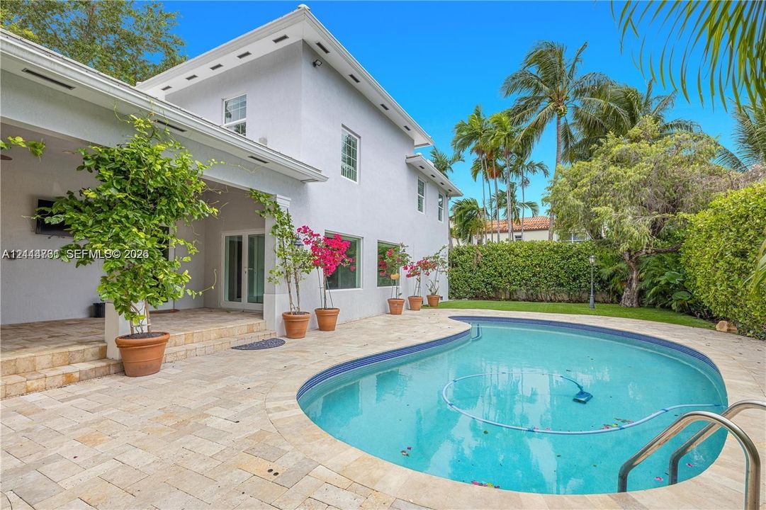 Covered terrace with stone tile flooring, freeform swimming pool, and manicured privacy hedge