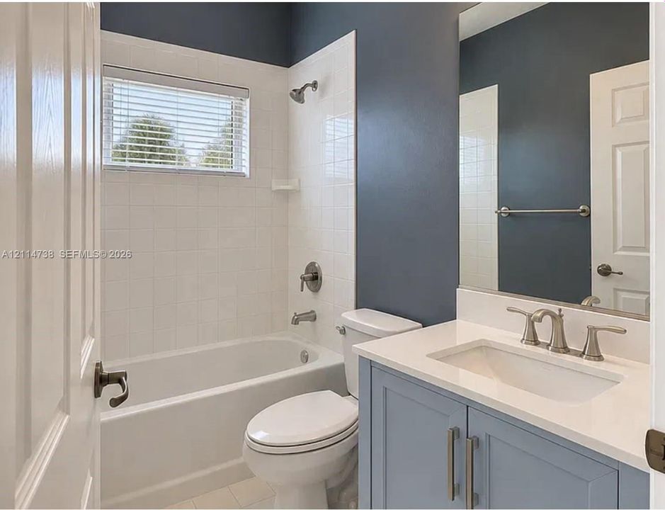 Bathroom featuring a vanity with a white countertop and undermount sink, a shower-tub combination with white tile surround, and a large wall-mounted mirror