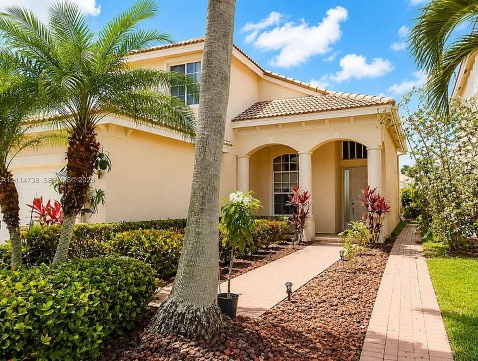 Two-story stucco exterior featuring a covered entryway with arched openings and structural columns, a tile roof, and a paved walkway