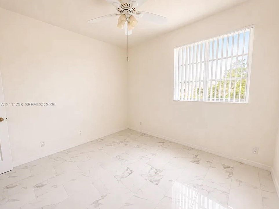 Neutral interior space featuring polished stone-finish flooring, a ceiling fan with integrated lighting, and a large window with vertical blinds