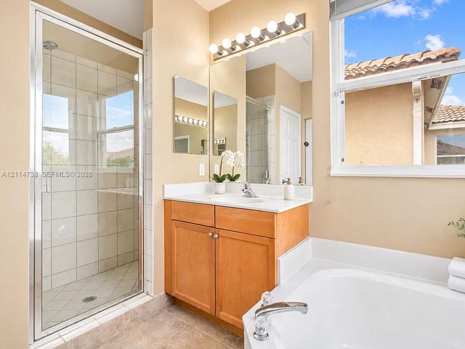 Bathroom featuring a glass-enclosed shower with tiled surround, wood-finish cabinetry, a white countertop with an integrated sink, a built-in soaking tub, and an expansive wall-mounted vanity mirror