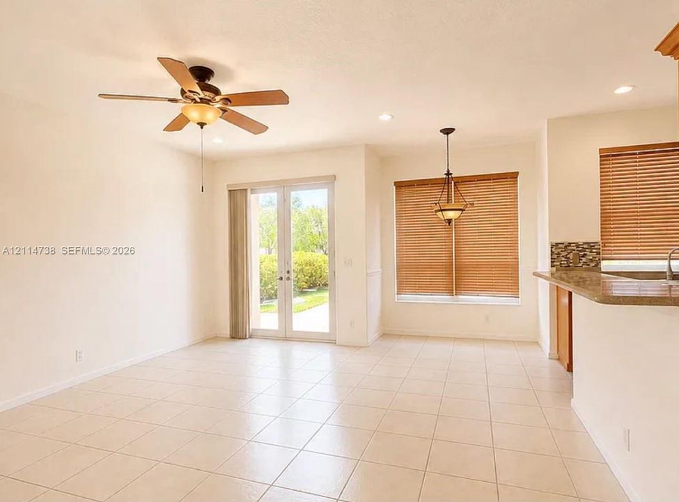 Neutral ceramic tile flooring, ceiling fan with integrated lighting, glass-paneled double doors, recessed lighting, and breakfast bar with stone-finish countertop