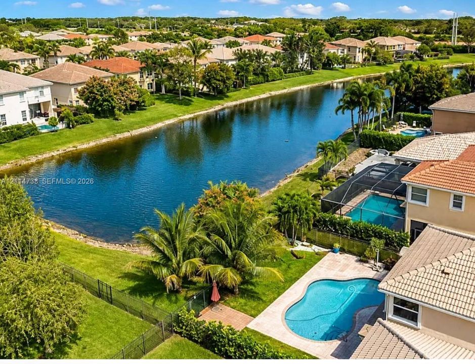 Aerial perspective of a property featuring a pool with paver decking, a manicured lawn, established palm trees, and water frontage