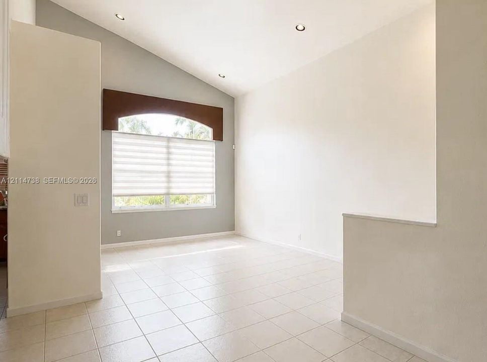 Vaulted ceiling with recessed lighting, tile flooring, and arched architectural window trim