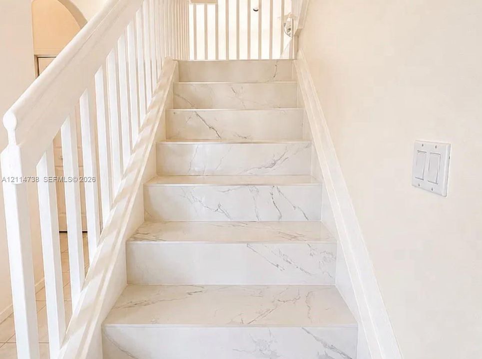Staircase featuring white stone-finish treads with veining detail and a white wood-finish railing with vertical balusters