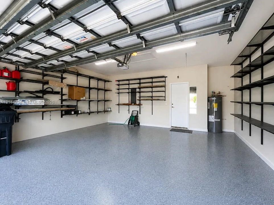 Garage featuring an epoxy-coated floor, extensive wall-mounted industrial shelving, recessed LED lighting, and direct exterior access via a side-entry door