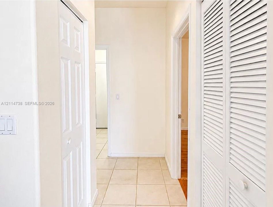 Neutral-toned ceramic floor tiling, white panel interior doors, and white louvered bifold closet doors