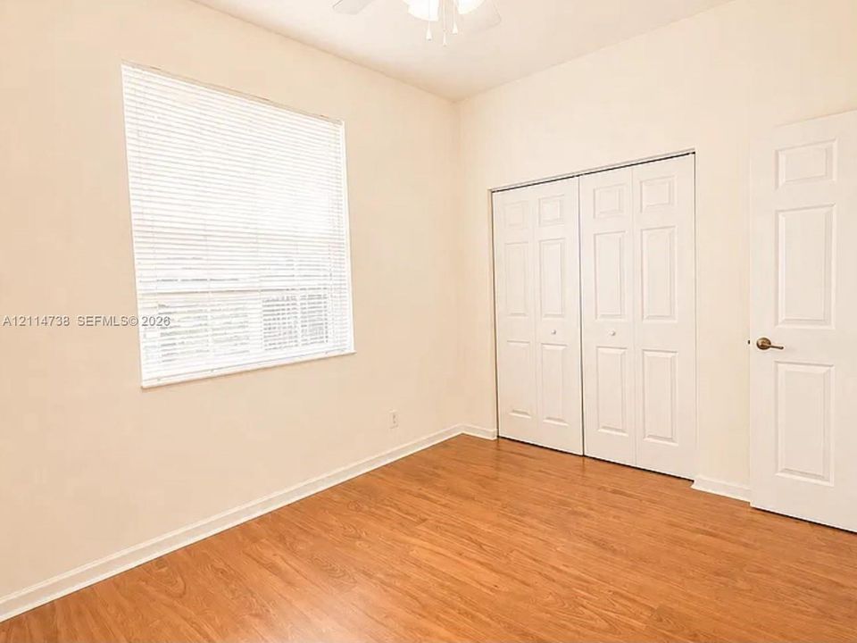 Room featuring wood-finish flooring, a window with horizontal blinds, ceiling fan, and double-door closet