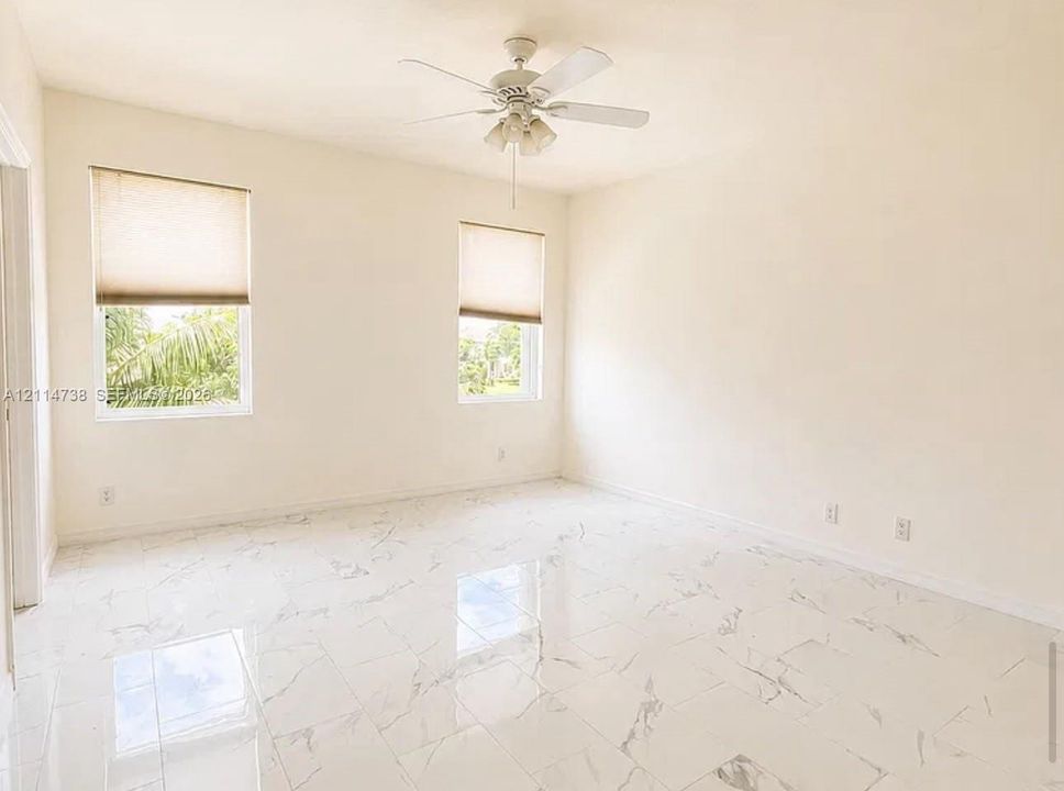 Interior space featuring polished white stone-patterned flooring, dual windows with fitted shades, and a ceiling-mounted fan with integrated lighting