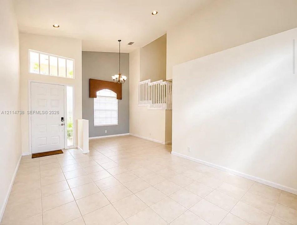 High-ceilinged entry featuring tile flooring, recessed lighting, multi-pane transom windows, a suspended chandelier, and a white balustrade