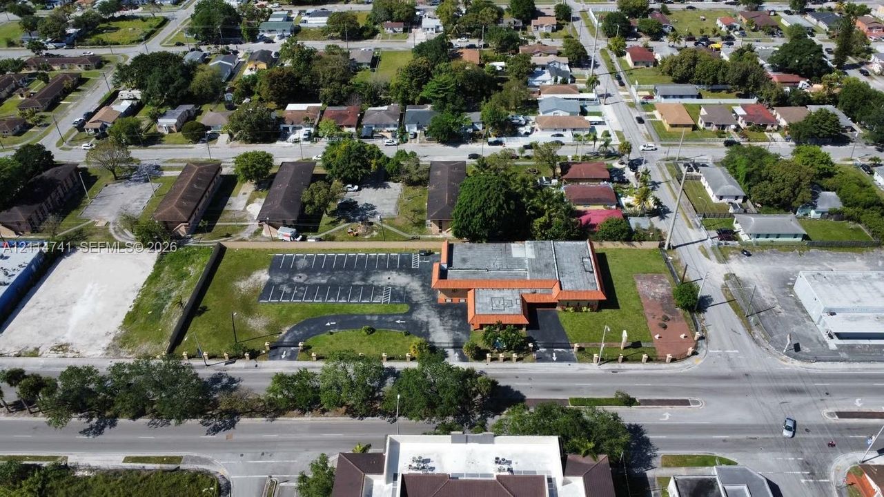 Aerial perspective of a corner lot property featuring a low-rise commercial structure, an expansive paved parking area, a dedicated drive-through lane, and perimeter landscaping