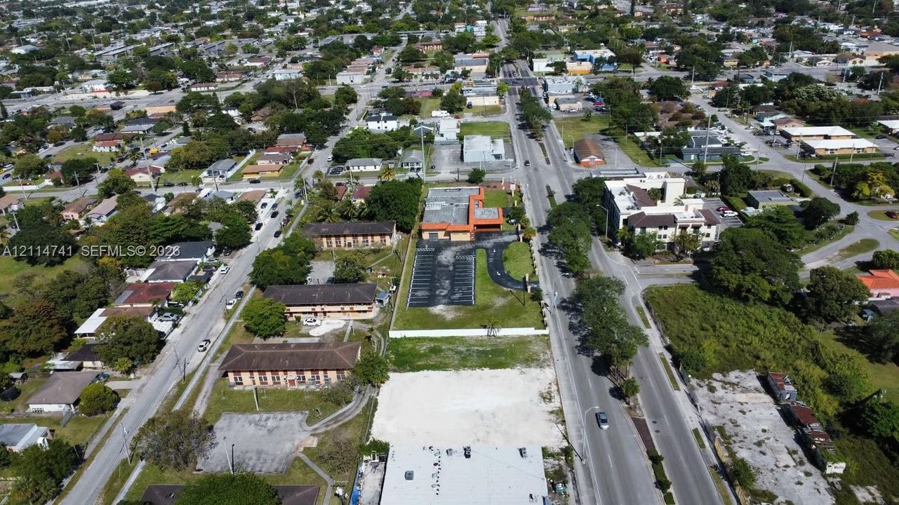 Aerial view of property featuring a flat-roofed structure, paved parking area, and accessible street frontage