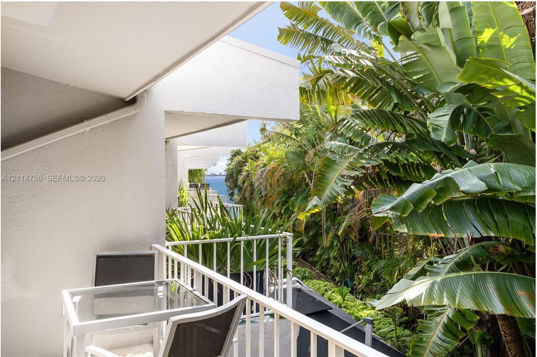 Covered balcony featuring white metal railings and mature tropical landscaping