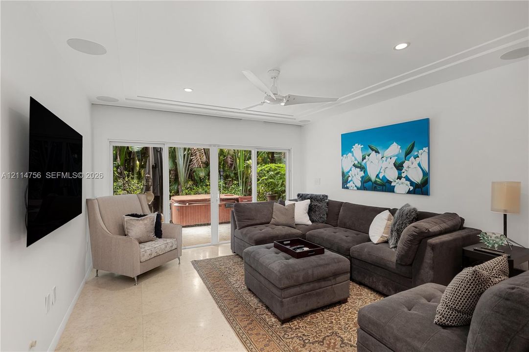 Living area featuring neutral stone flooring, crown molding, ceiling fan with integrated lighting, built-in ceiling speakers, and sliding glass doors