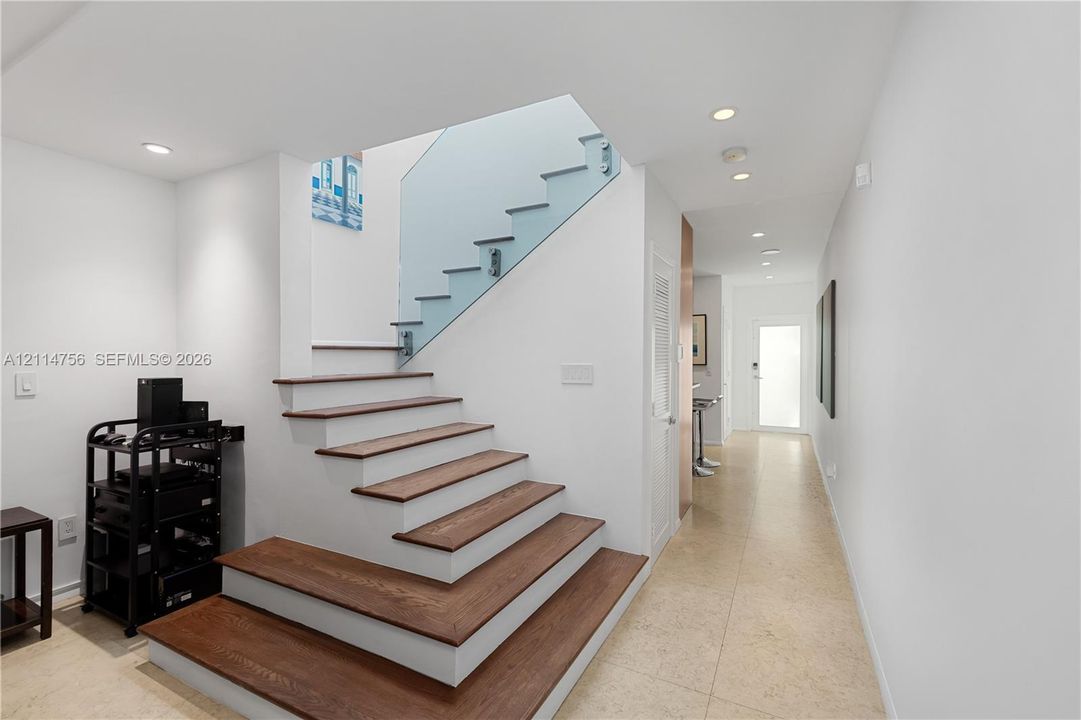 Staircase featuring wood-finish treads, glass panel railing with metallic mounts, recessed ceiling lighting, and tile flooring