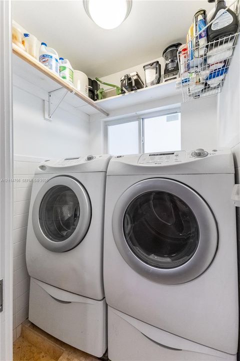 Laundry area featuring white subway tile wall cladding, fixed upper wood shelving, an operable window, and a flush-mount ceiling light fixture